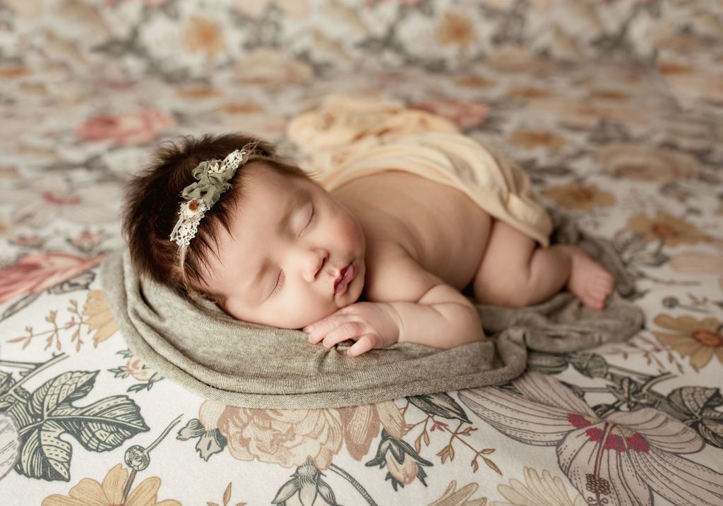 A newborn baby girl is sleeping on a floral blanket.