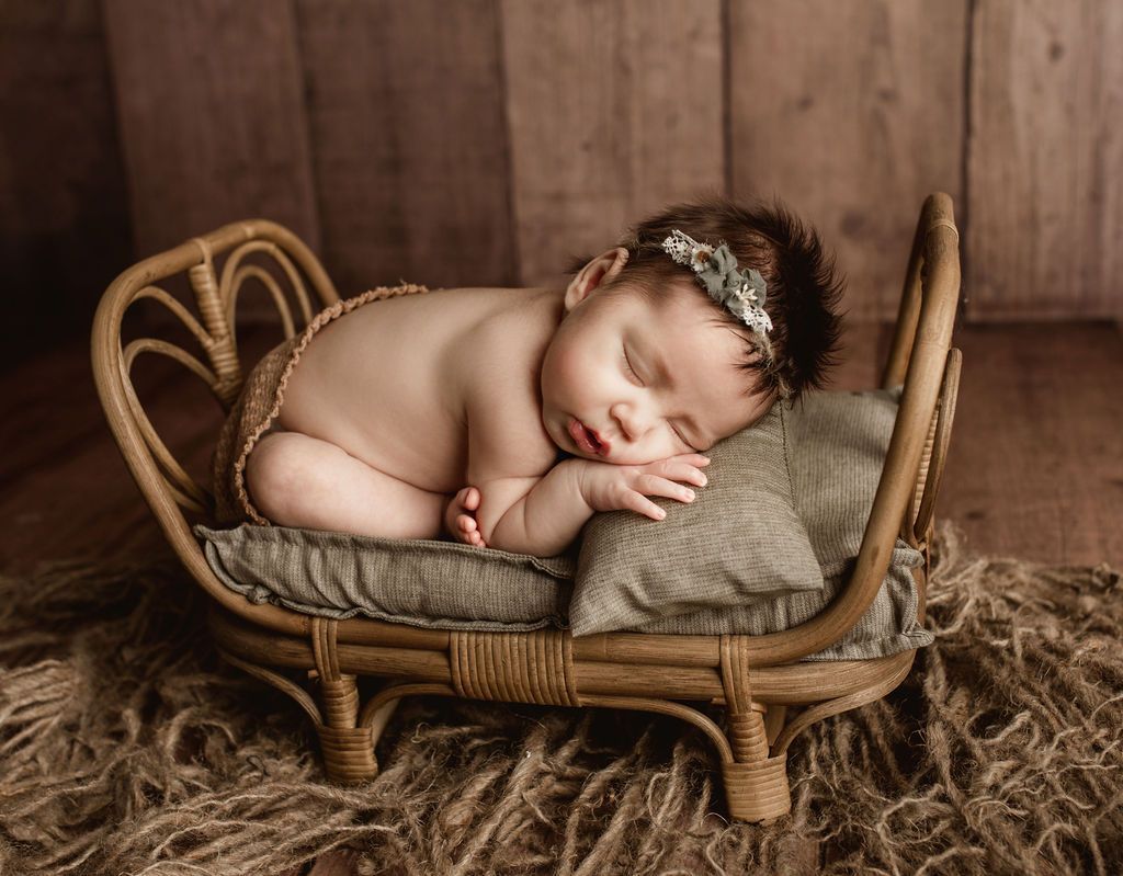 A newborn baby is sleeping in a wicker bed.