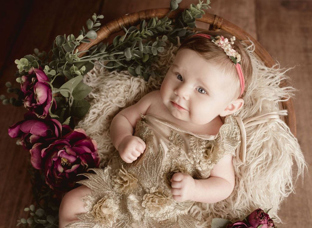 A baby is laying in a basket with flowers.