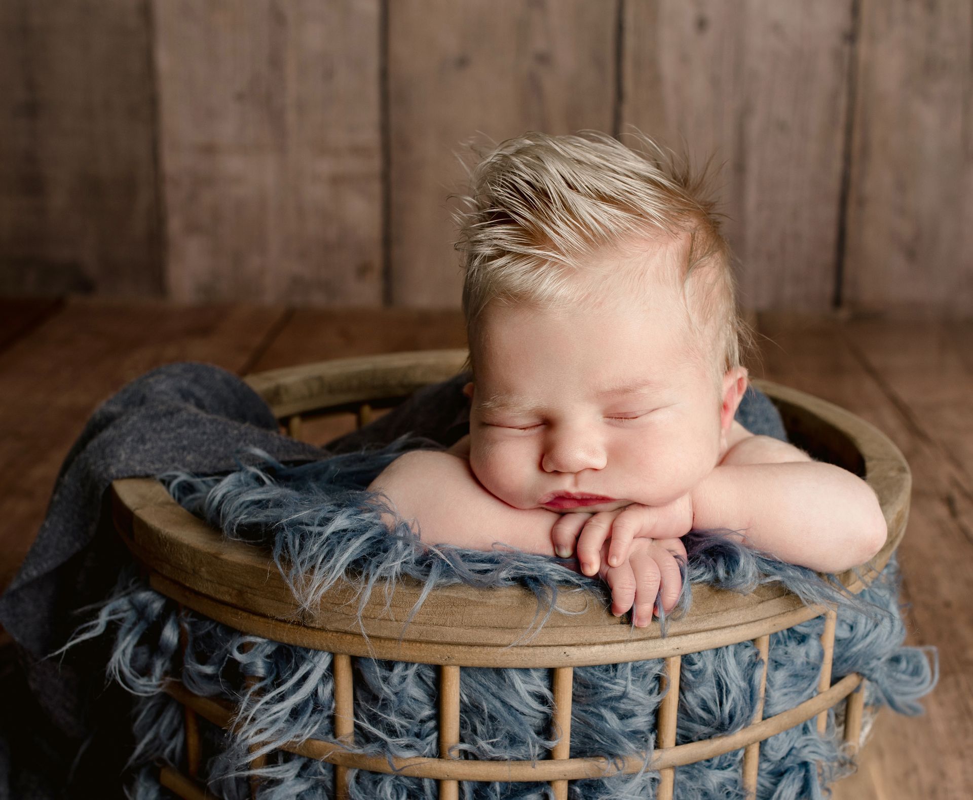 A newborn baby is sleeping in a wooden basket. Baby Studio with Props