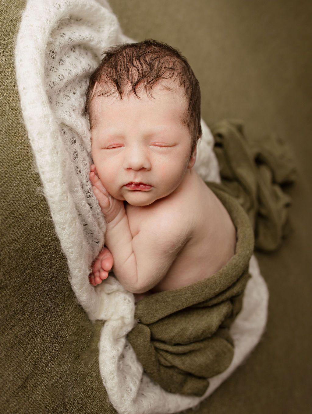 A newborn baby wrapped in a green and white blanket is sleeping. baby studio