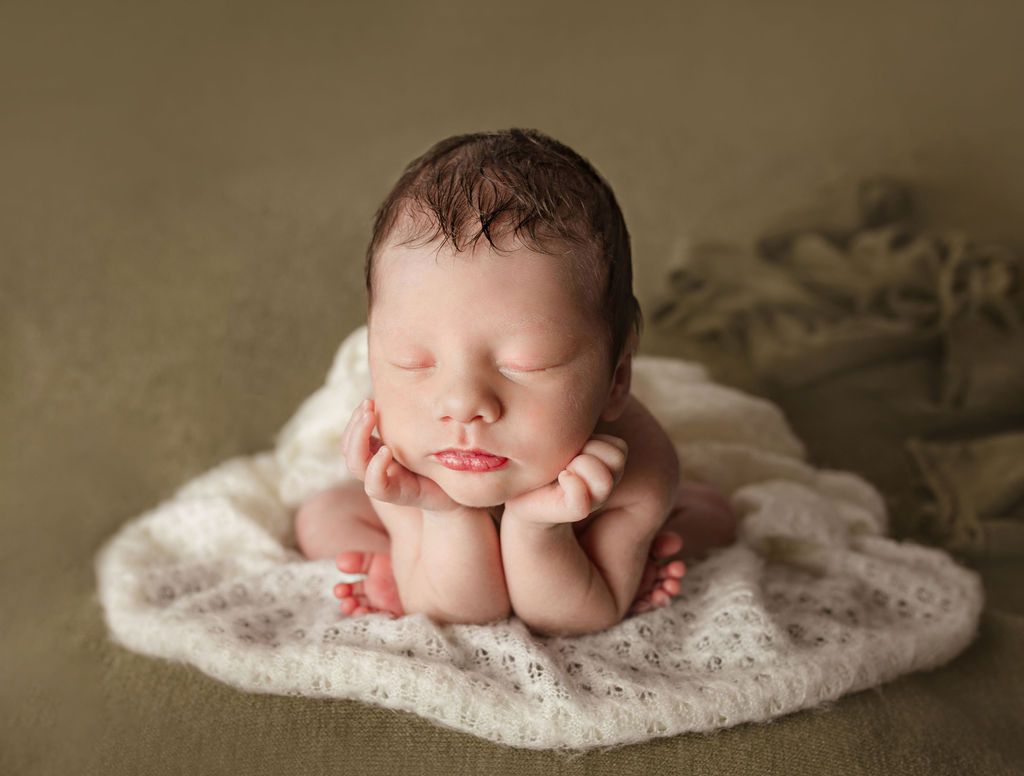A newborn baby is sleeping on a white blanket.