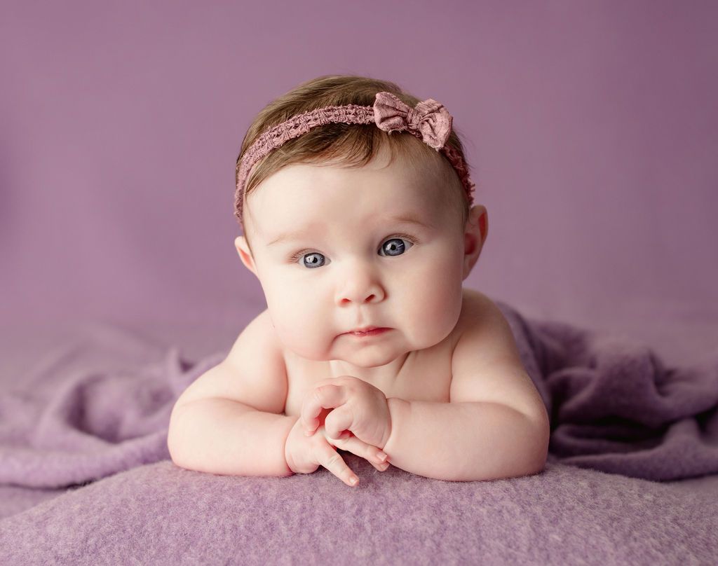 A baby girl is laying on her stomach on a purple blanket.