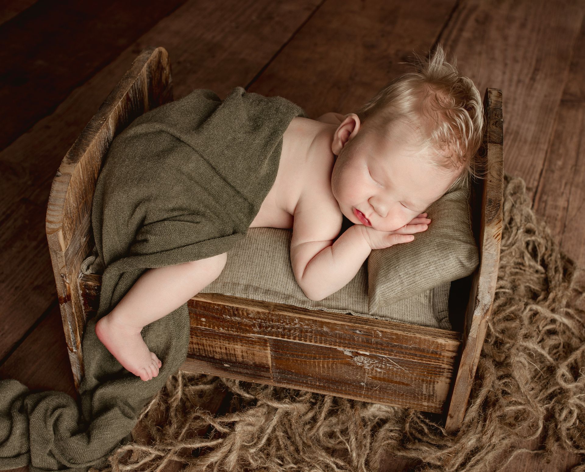 A baby is sleeping in a wooden crate on a wooden floor. Baby Studios with Props