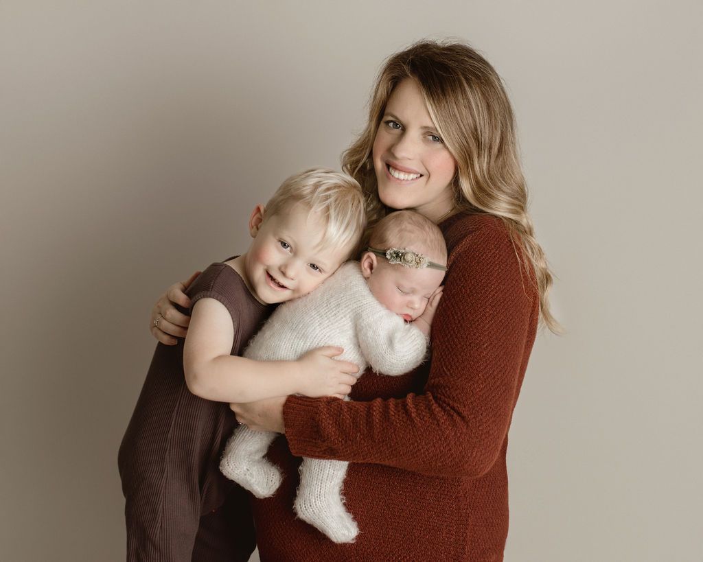 A woman is holding two children , one of whom is a newborn baby.