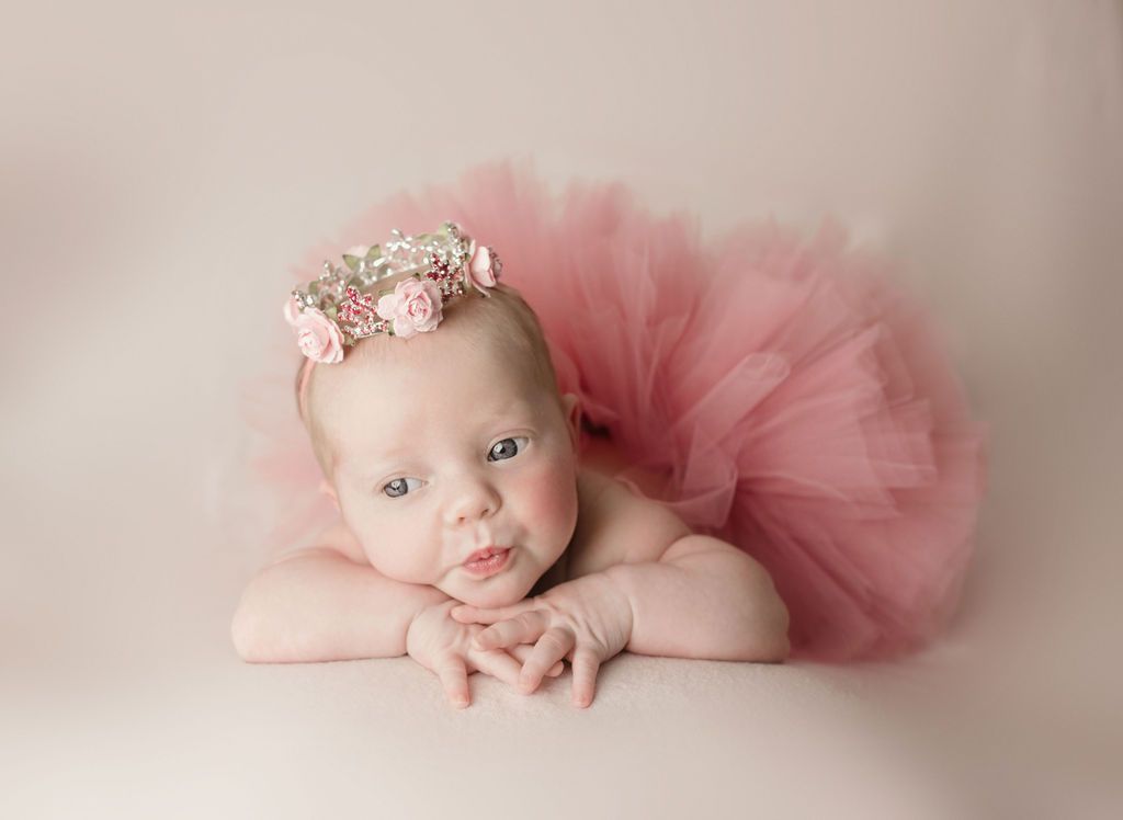 A baby girl is wearing a pink tutu and a flower crown.