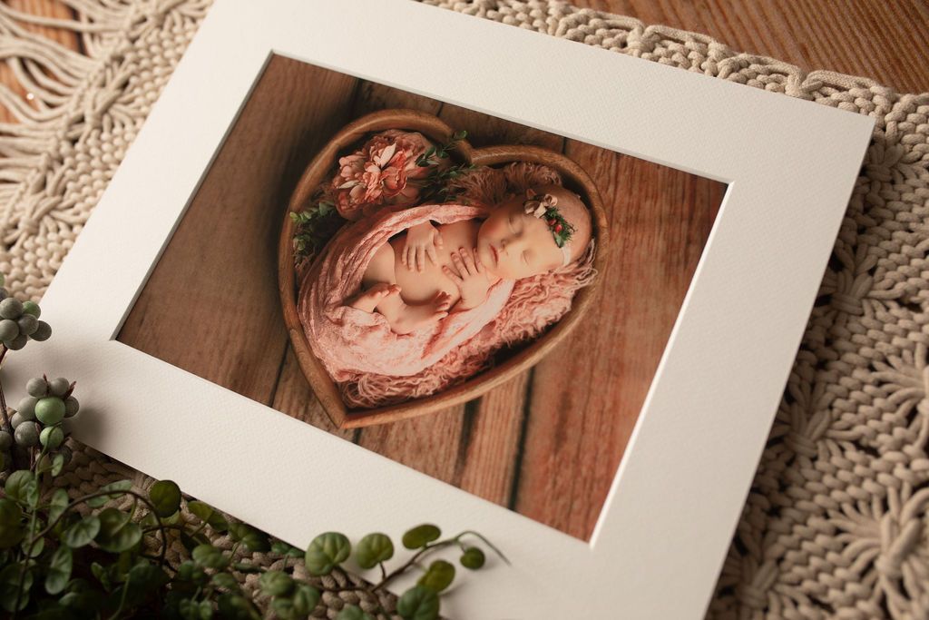 A picture of a baby in a heart shaped bowl on a wooden table.