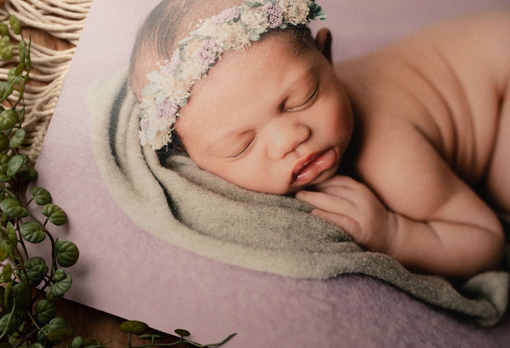 A newborn baby wearing a flower crown is sleeping on a blanket.