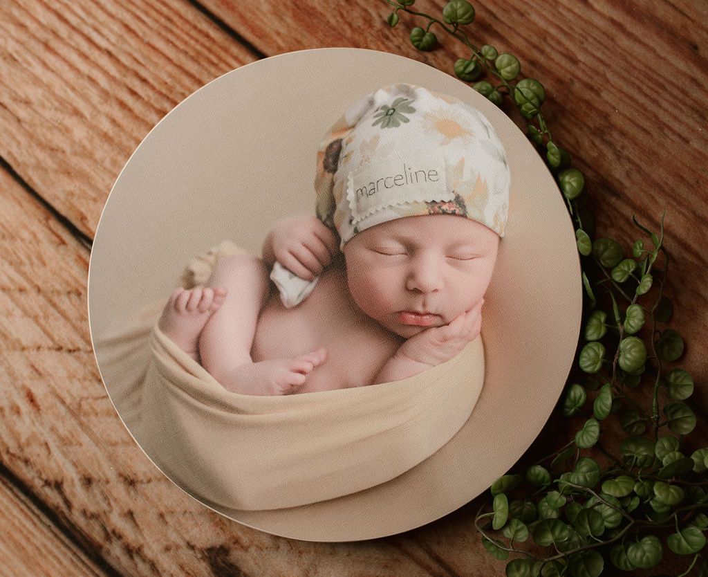 A newborn baby wearing a hat is sleeping on a wooden table.