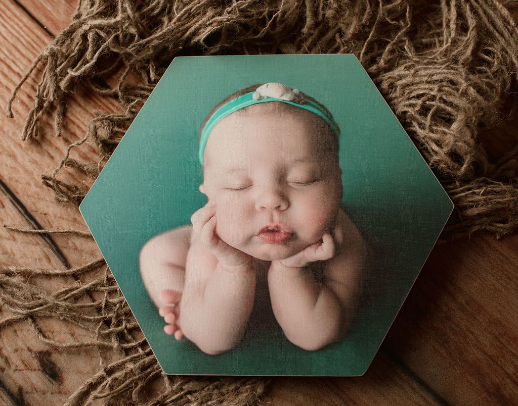 A baby is laying on a wooden table with his hands on his face.