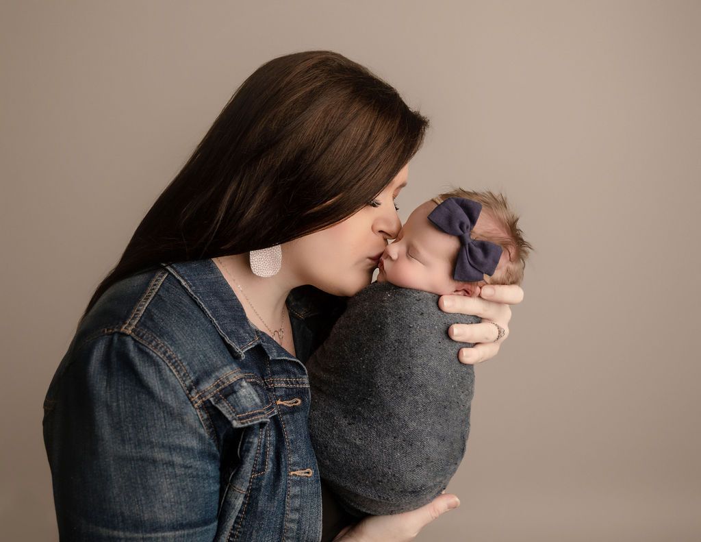 A woman is kissing her newborn baby on the cheek.