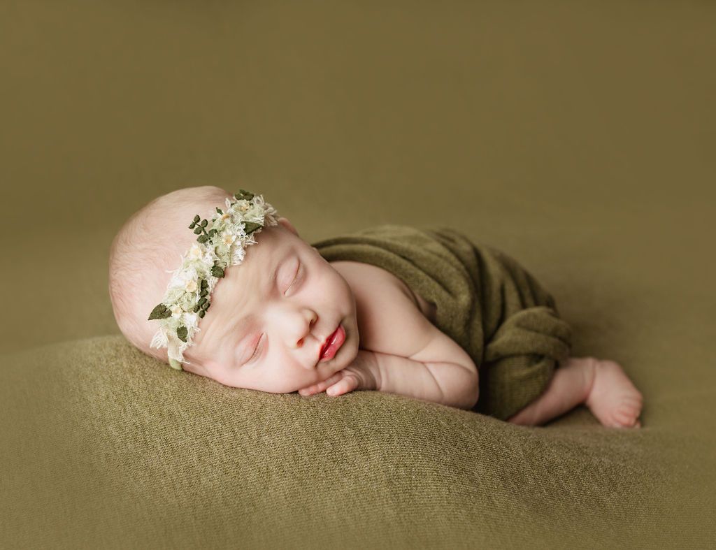 A newborn baby wearing a flower crown is sleeping on a blanket.