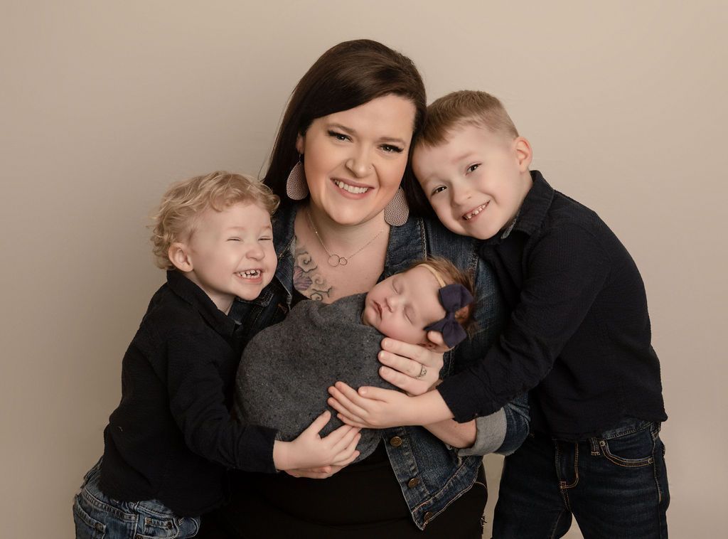 A woman is holding a newborn baby and two boys are hugging her.