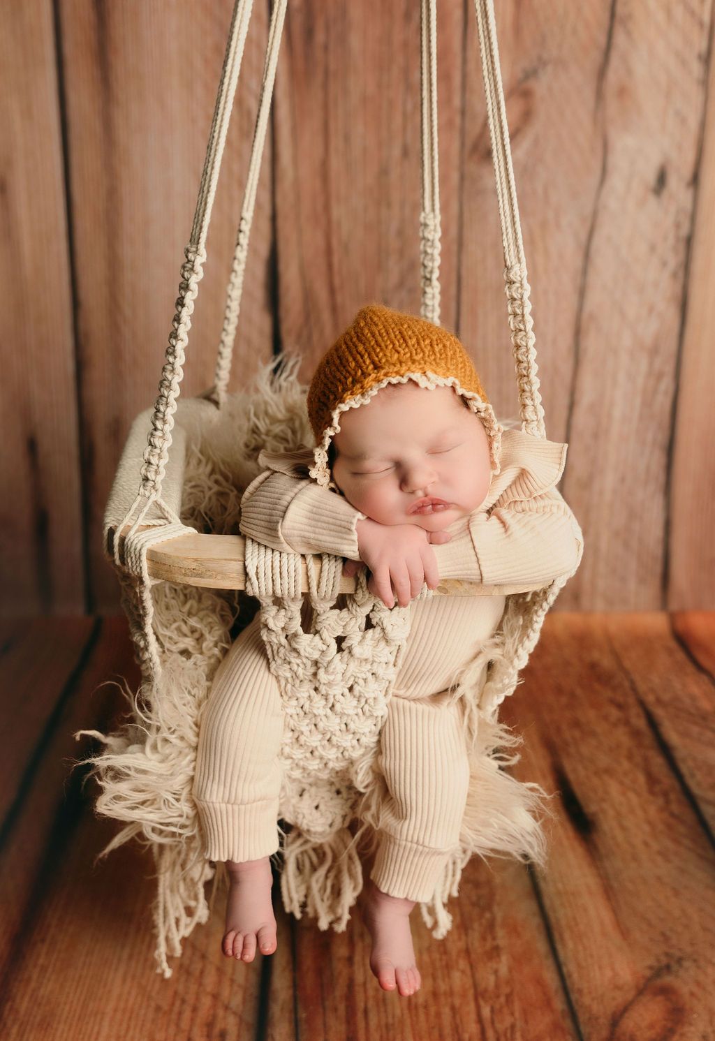 A baby is sleeping in a swing on a wooden floor.