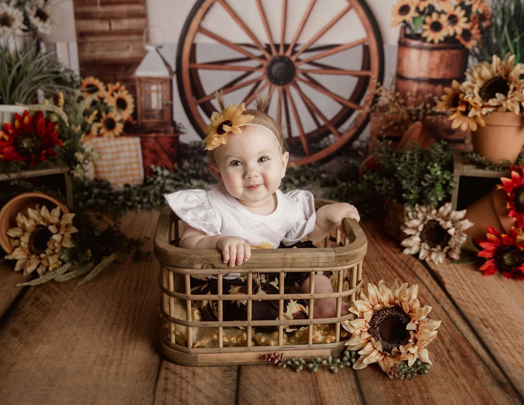 A baby is sitting in a wooden basket surrounded by sunflowers.