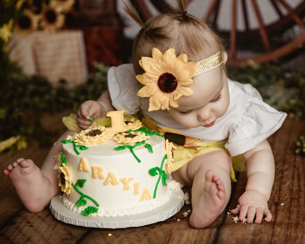A baby is sitting on a wooden floor next to a cake.