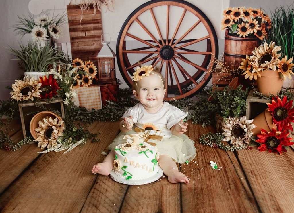 A baby girl is sitting on a wooden floor eating a cake.
