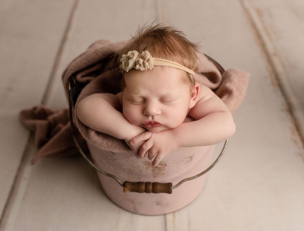 A newborn baby is sleeping in a pink bucket.