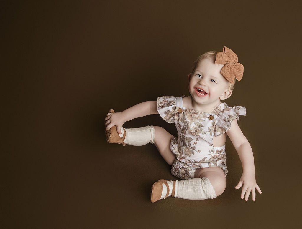 A baby girl is sitting on the floor and smiling.