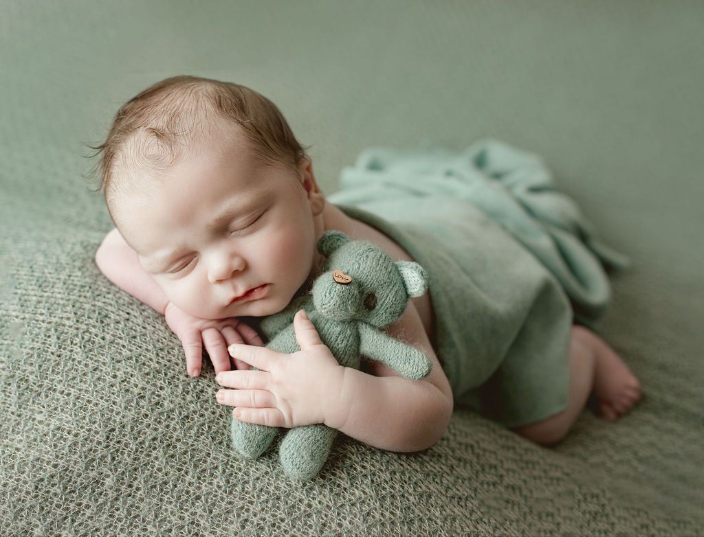 A newborn baby is laying on a blanket holding a teddy bear.