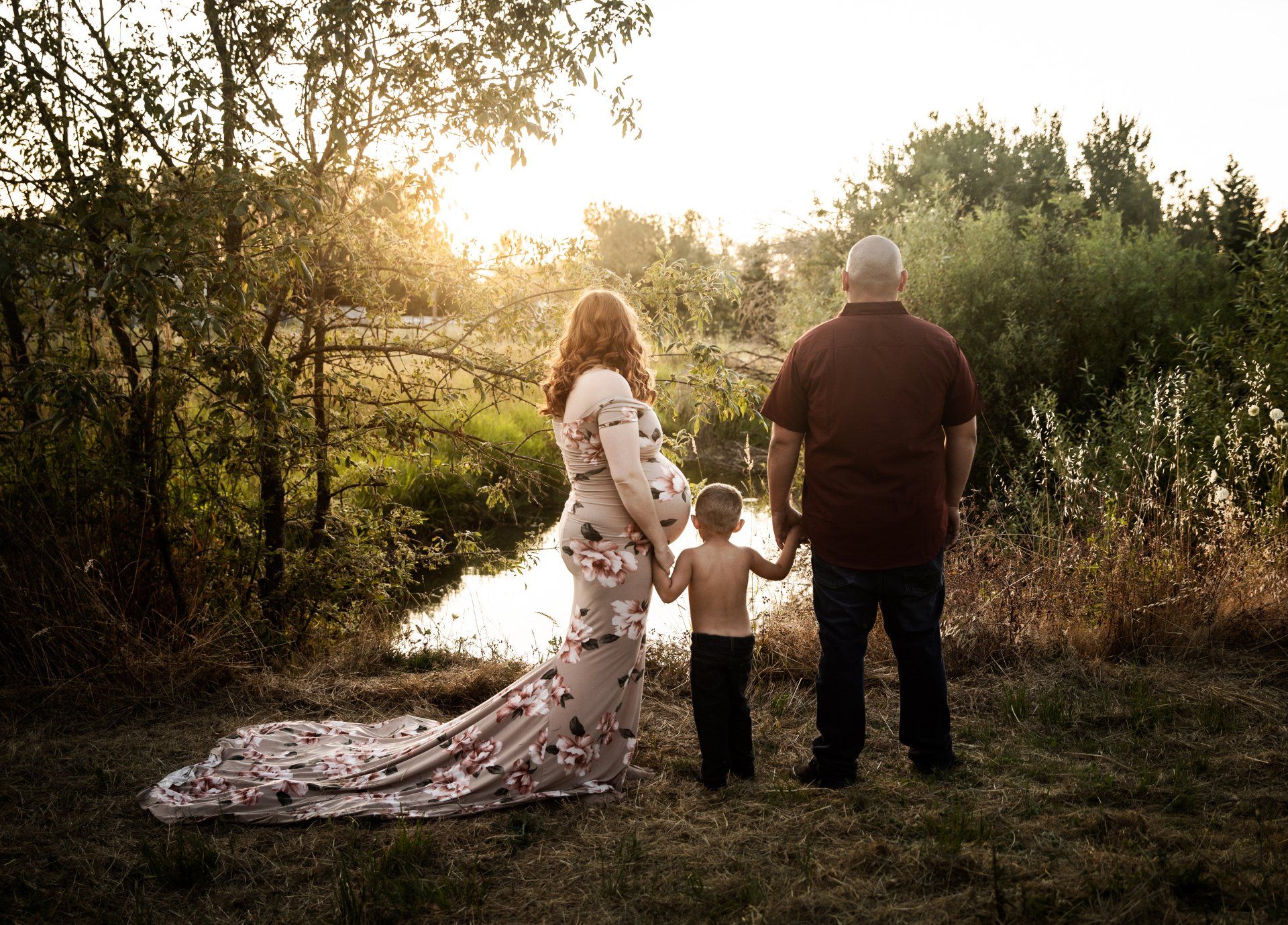 A pregnant woman is standing next to a man and a child holding hands.