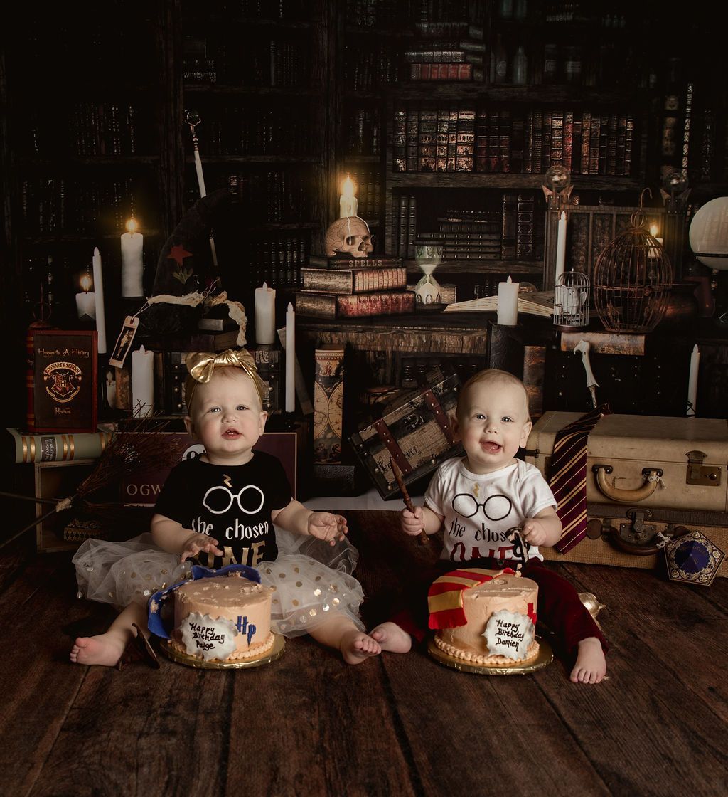 Two babies are sitting next to each other on a wooden floor holding cakes.
