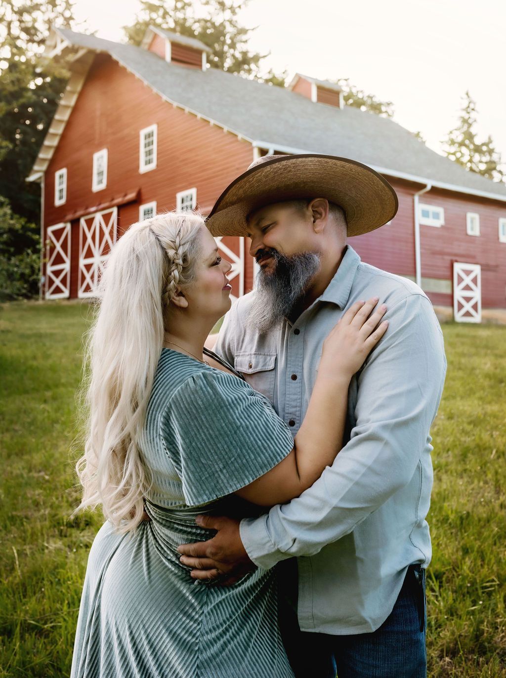 A man and a woman are hugging in front of a red barn.