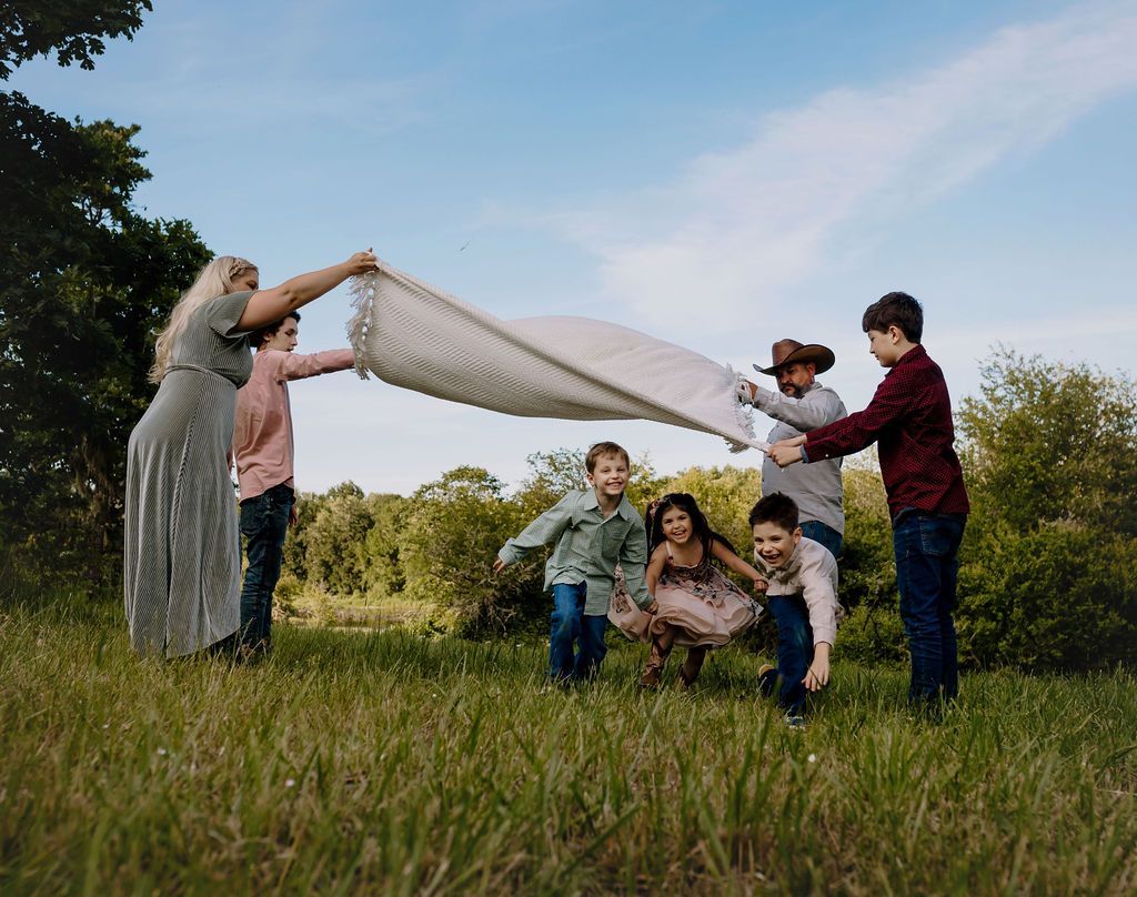 A group of people are playing with a blanket in a field.