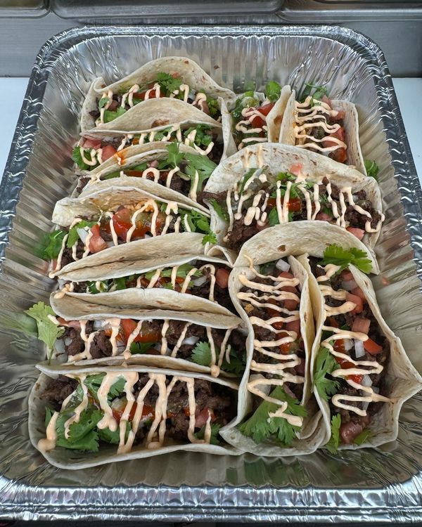 A tray of tacos with tomatoes , lettuce , and mayonnaise on a table.