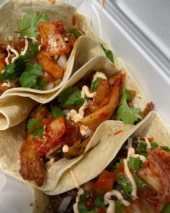 Three tacos are sitting on top of each other in a styrofoam container.