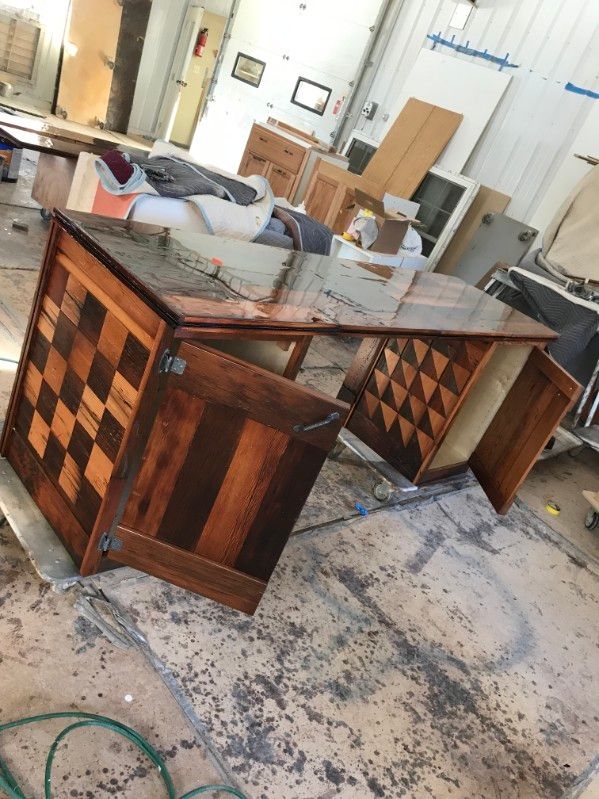 Wooden desk with checkerboard-patterned sides and dark, glossy finish in a workshop setting. Wooden desk with checkerboard-patterned sides and dark, glossy finish in a workshop setting.