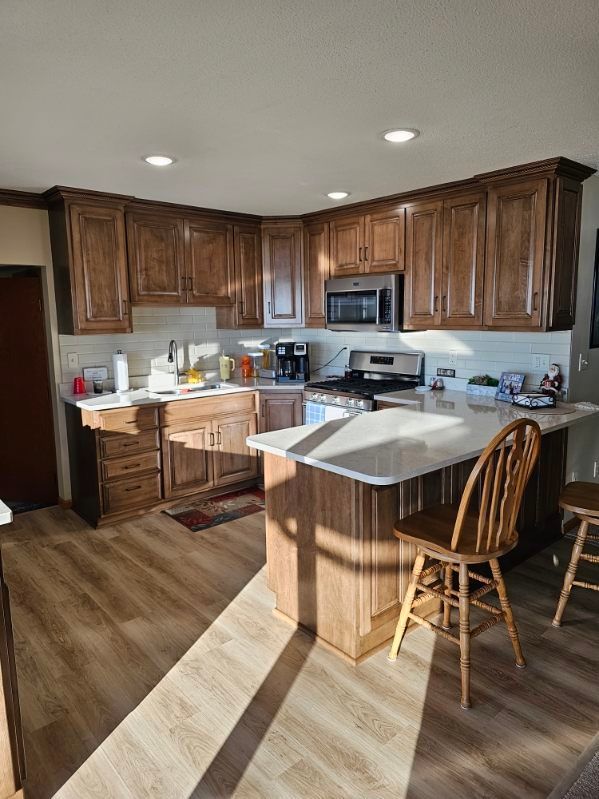 Kitchen with brown cabinets, white countertops, and wood-look flooring. Sunlight streams in. Kitchen with brown cabinets, white countertops, and wood-look flooring. Sunlight streams in.