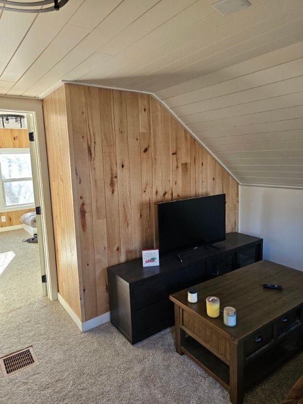 Living room with wood paneling, TV, coffee table, and carpet. Doorway to another room visible.