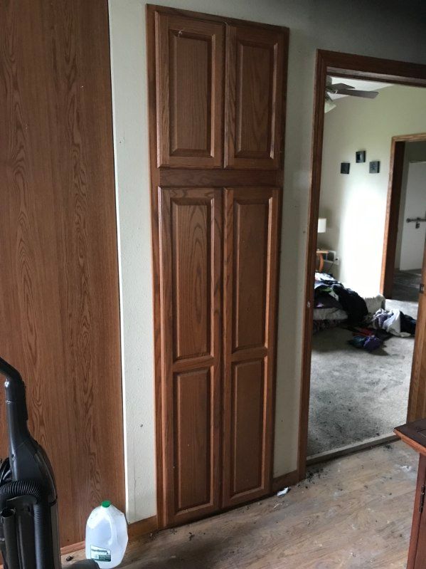 Tall wooden cabinet with two sets of doors, set in a light-colored wall. A doorway is visible to the right.