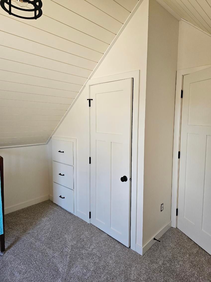 A room with white sloped ceiling, built-in drawers, closet doors, and gray carpet.