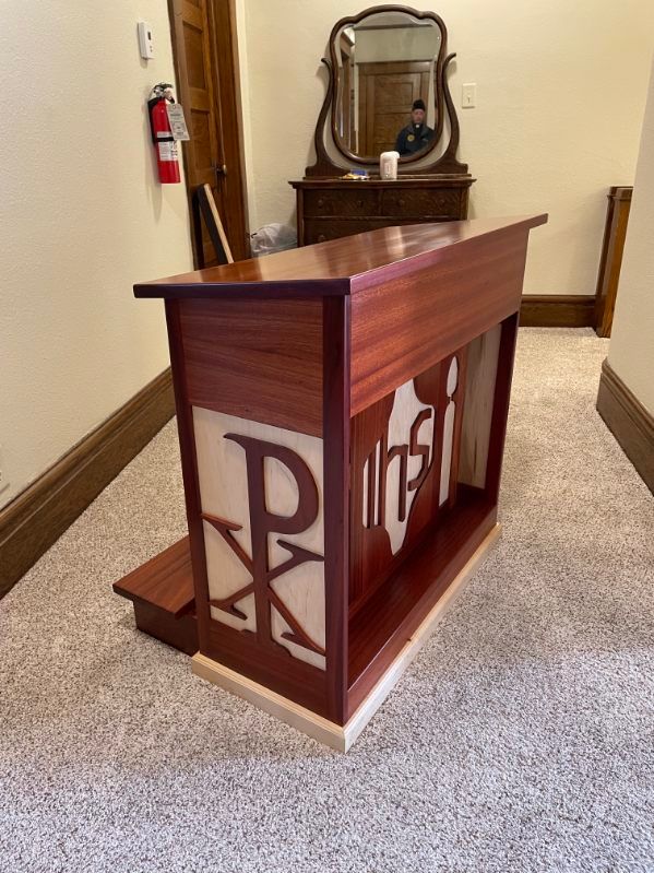 Wooden lectern with a carved design in a hallway.