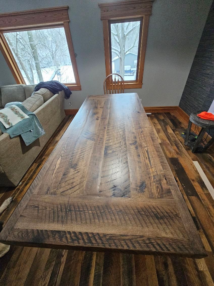 Large, weathered wooden dining table in a room with hardwood floors and windows overlooking a snowy landscape. Large, weathered wooden dining table in a room with hardwood floors and windows overlooking a snowy landscape.