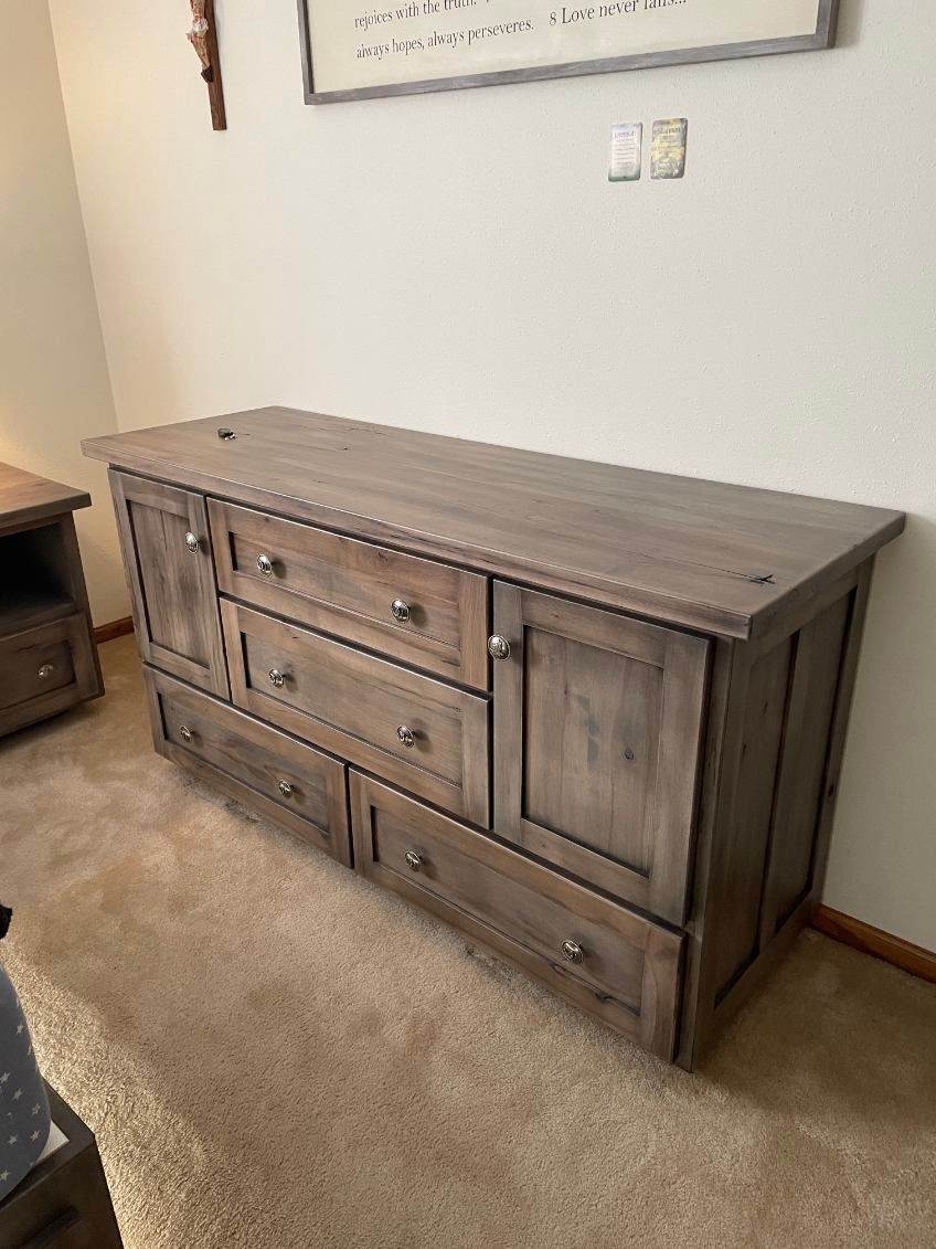 Wooden dresser with multiple drawers and cabinets, set on a carpeted floor against a wall.