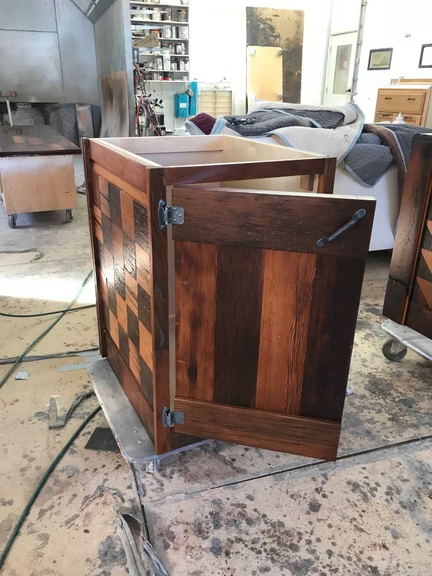 Wooden cabinet with open door; dark and light stained wood, checkered pattern. Workshop setting.