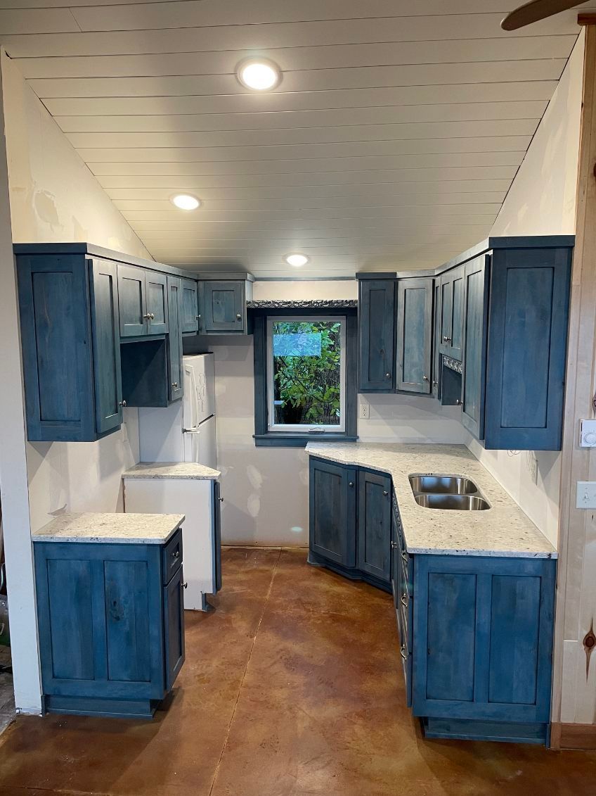 Blue cabinets in a small kitchen with white countertops and a window.