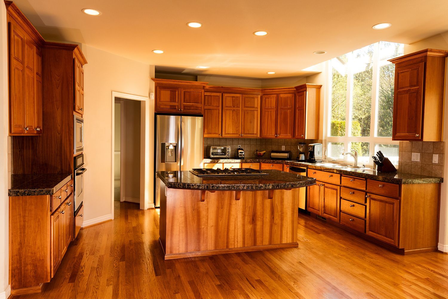 Wooden kitchen with an island, cabinets, appliances, and large windows.
