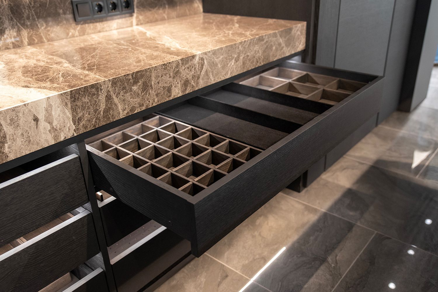 Black kitchen drawer open, revealing storage compartments against a marbled countertop. Black kitchen drawer open, revealing storage compartments against a marbled countertop.