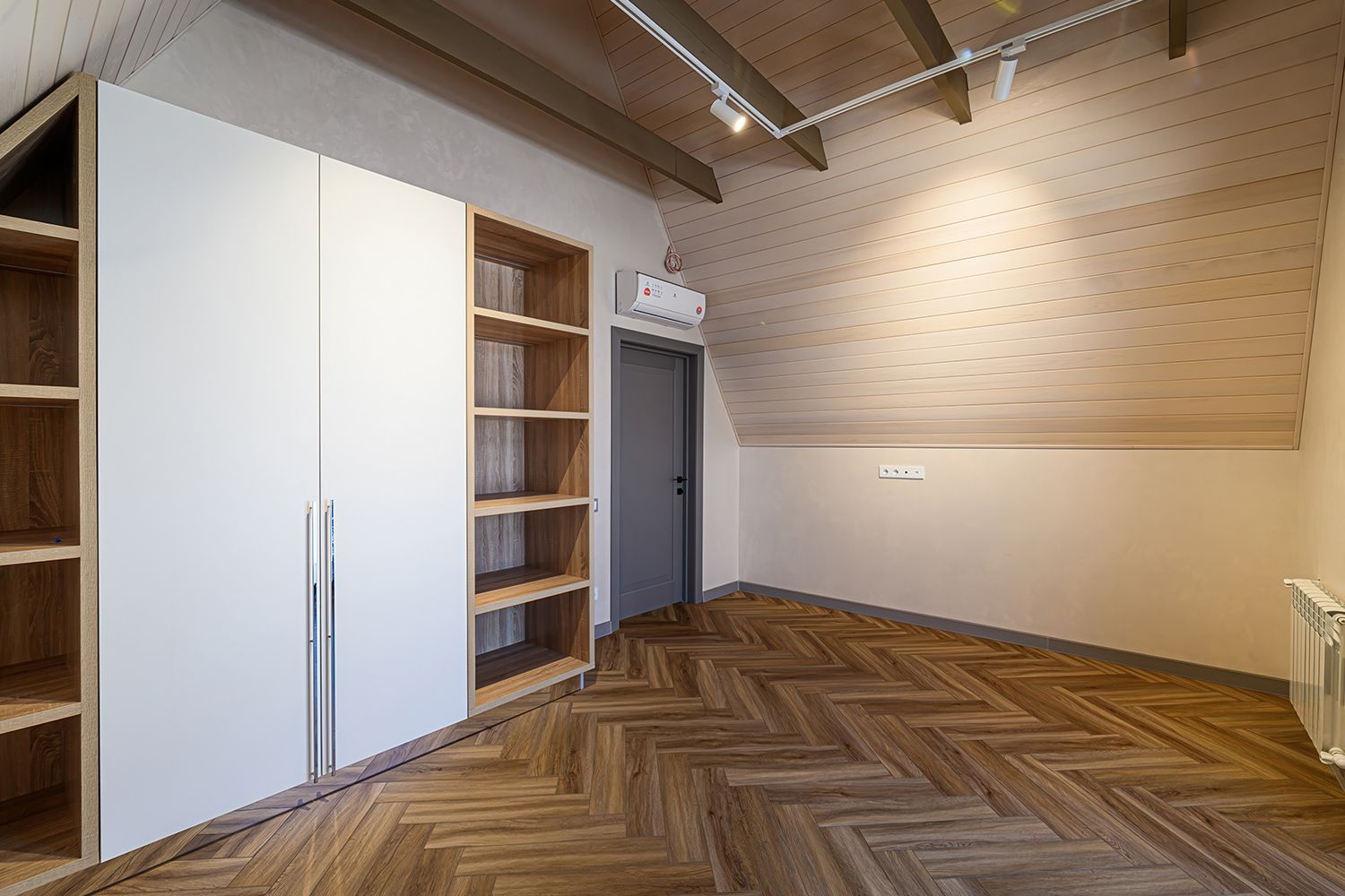 Wooden-floored room with white closet, open shelves, gray door, and slanted, wood-paneled ceiling.