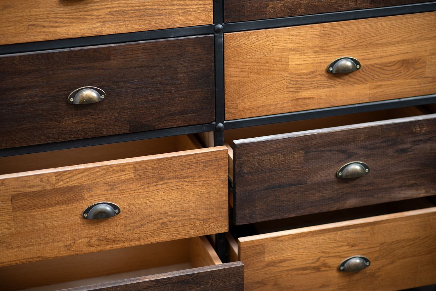 Wooden dresser with various open and closed drawers, featuring bronze handles and a two-tone wood stain. Wooden dresser with various open and closed drawers, featuring bronze handles and a two-tone wood stain.