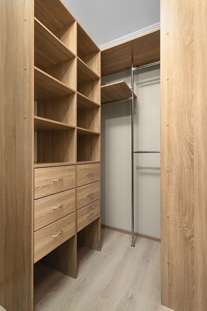 Walk-in closet with light wood shelving, drawers, and hanging rod. Light-colored flooring and walls.