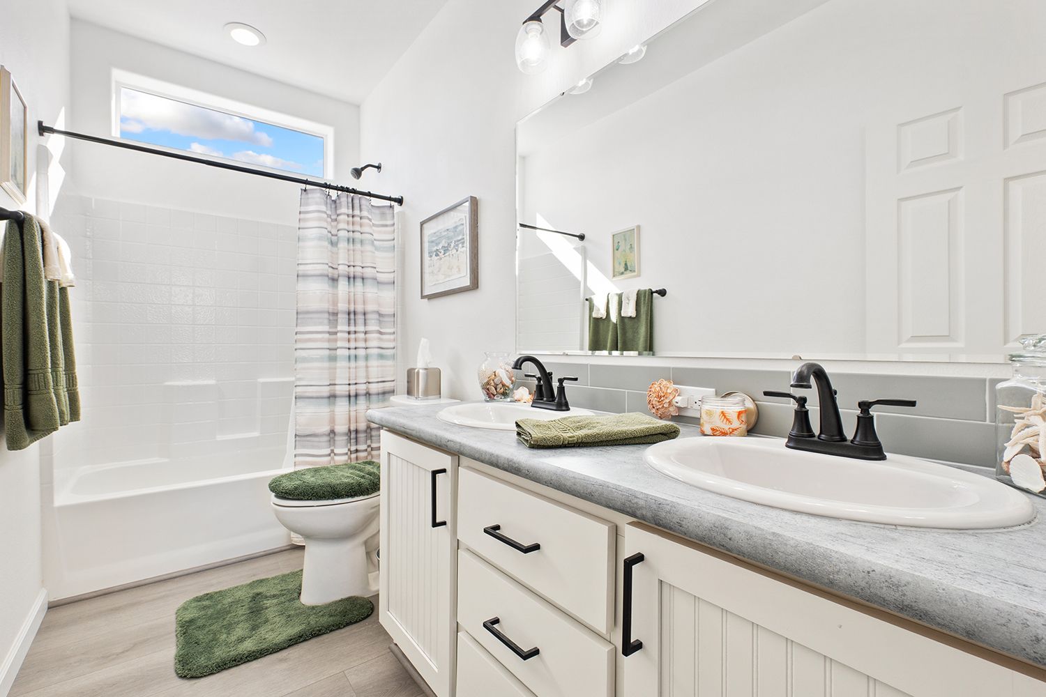 Bathroom with white vanity, double sinks, bathtub, toilet, green accents, and a window. Bathroom with white vanity, double sinks, bathtub, toilet, green accents, and a window.