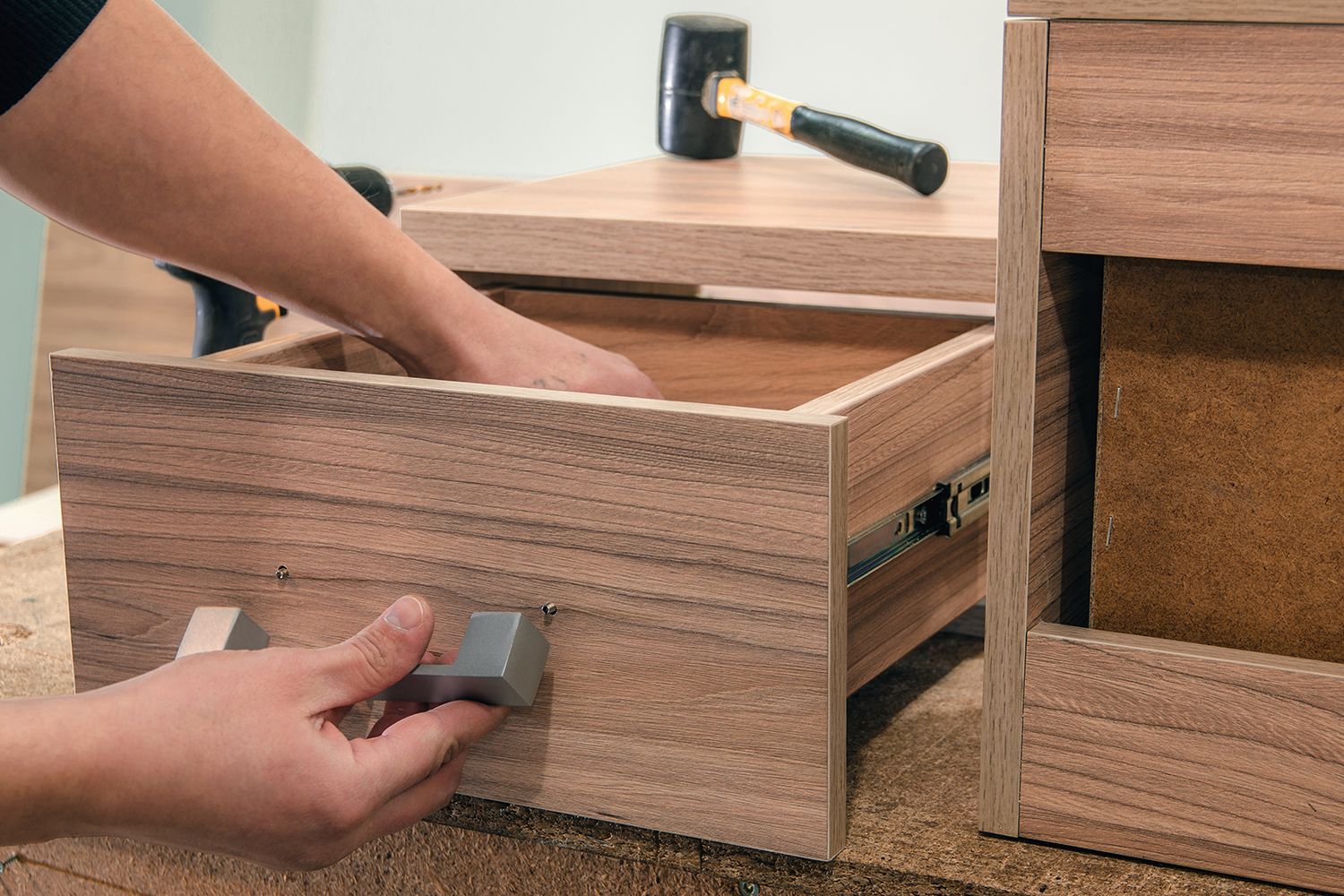 Person assembling a wooden drawer, with a hammer in the background. Person assembling a wooden drawer, with a hammer in the background.