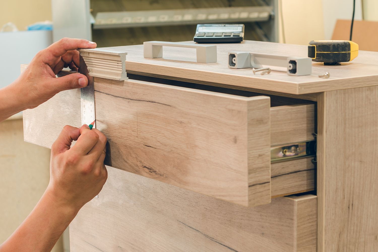 Person installing drawer front on a light wood cabinet with silver hardware. Person installing drawer front on a light wood cabinet with silver hardware.