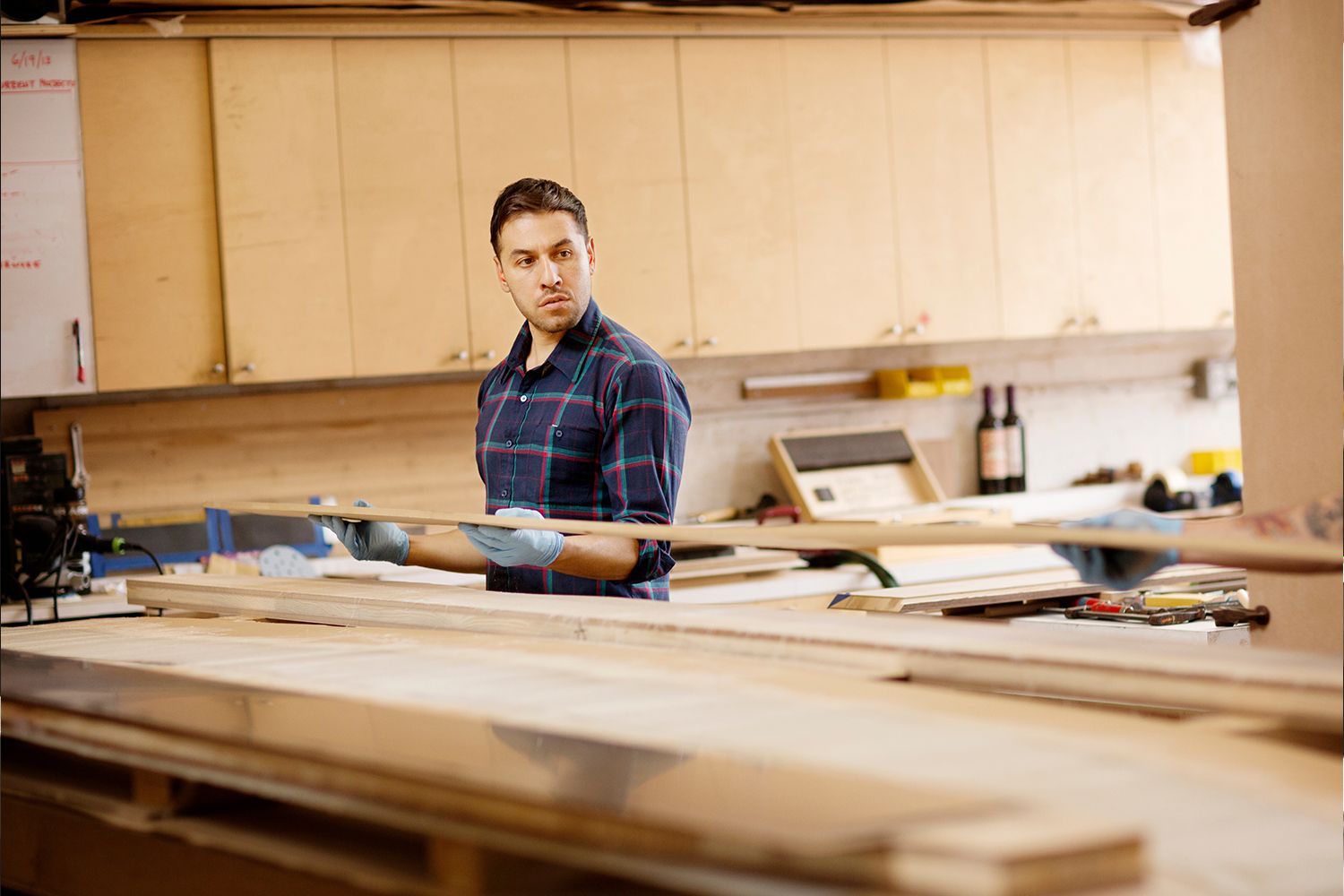 Man in blue plaid shirt looks over shoulder while working with wood in a workshop. Man in blue plaid shirt looks over shoulder while working with wood in a workshop.