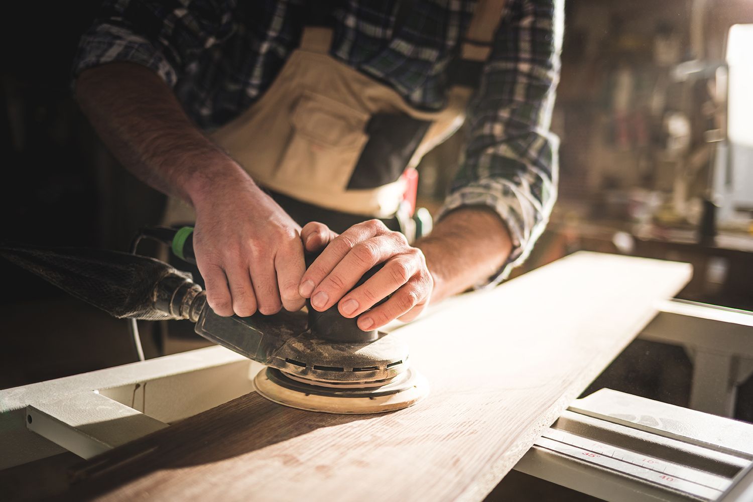 Person using a sander on a wooden plank in a workshop. Person using a sander on a wooden plank in a workshop.